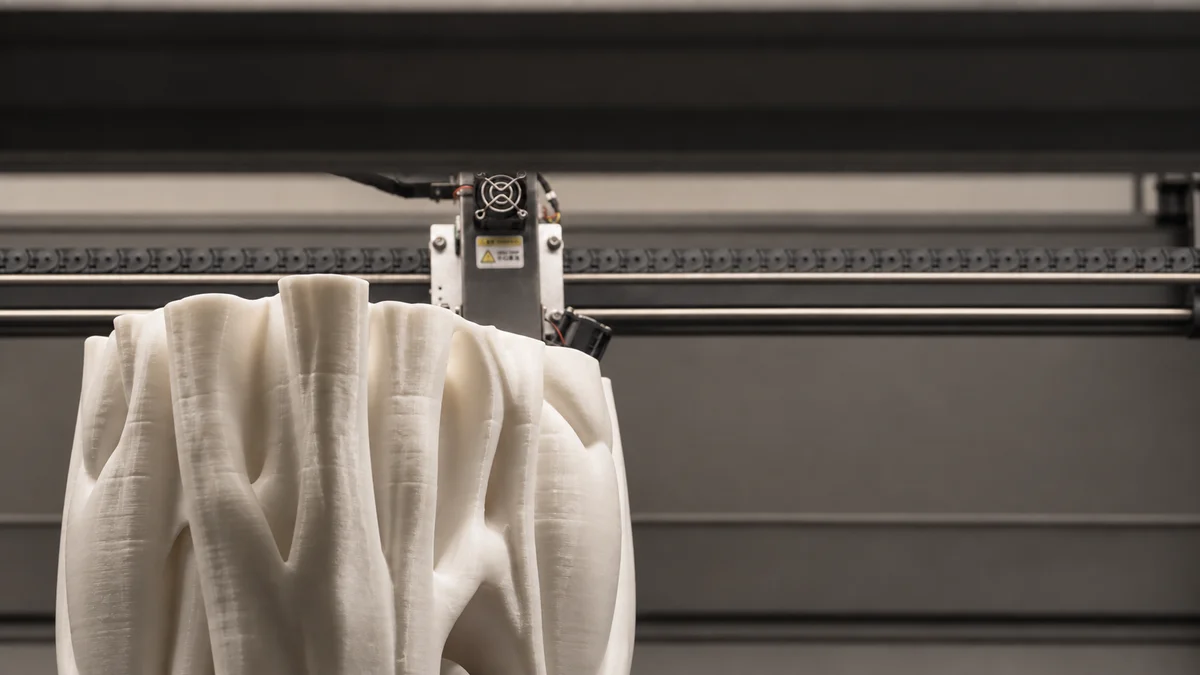 Close view of a pale sculptural form being made inside a fabrication machine.